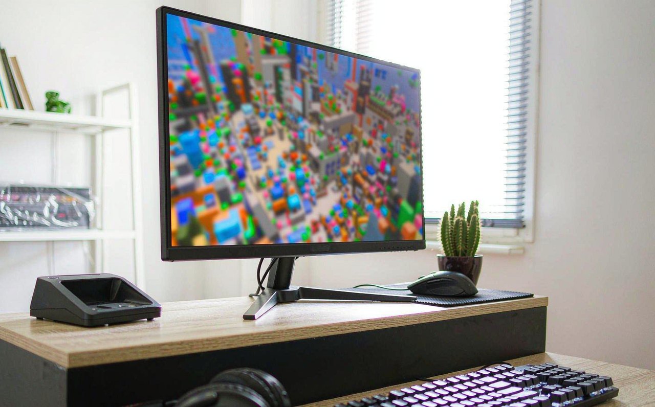 A gaming setup with a monitor showing a colorful blurred blocky game world, keyboard and mouse on a bright desk