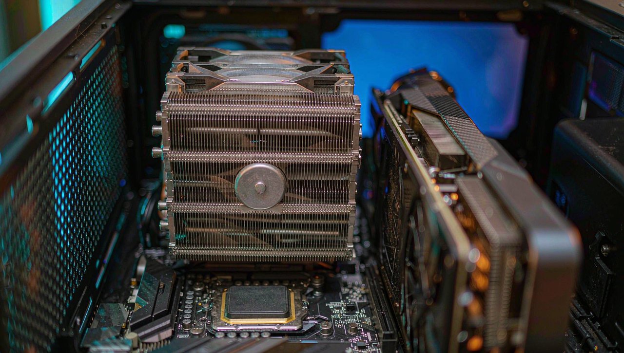 The inside of an open gaming PC with a large tower CPU cooler lit by cyan and amber fan lighting